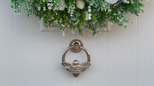 Bee-shaped silver door knocker on white door.